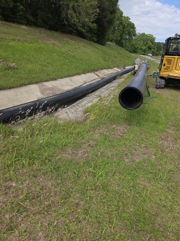 HDPE pipe staged along roadside with excavator