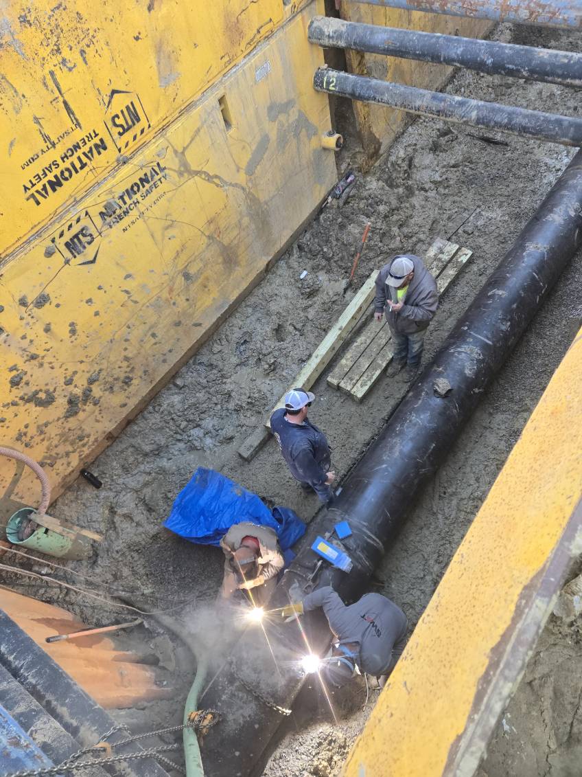 Workers preparing utility pipe in a shored trench